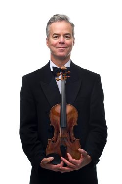Editorial portrait of Frank Almond, former Milwaukee Symphony Orchestra concertmaster, holding his historic Stradivarius violin in a black tuxedo against a white studio backdrop.