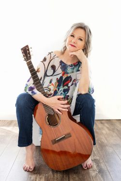 Personal branding portrait of a Southern Wisconsin singer-songwriter and cover artist seated barefoot with an acoustic guitar, photographed against a white backdrop at Jennifer Brindley Portrait.